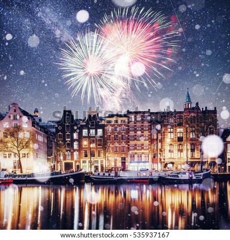 Beautiful night in Amsterdam. Night illumination of buildings and boats near the water in the canal. Photo greeting card. Colorful fireworks on the black sky background