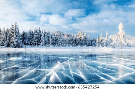 Blue ice and cracks on the surface of the ice. Frozen lake under a blue sky in the winter. The hills of pines. Winter. Carpathian, Ukraine, Europe