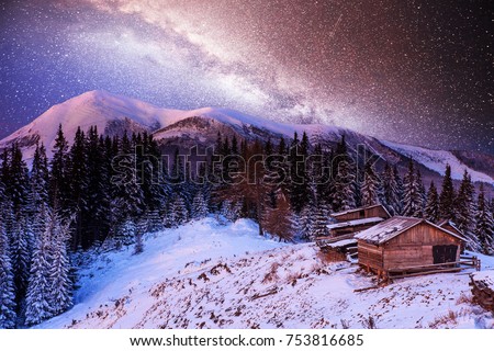 magical winter snow covered trees and mountain village. Winter landscape. Vibrant night sky with stars and nebula and galaxy. Deep sky astrophoto.