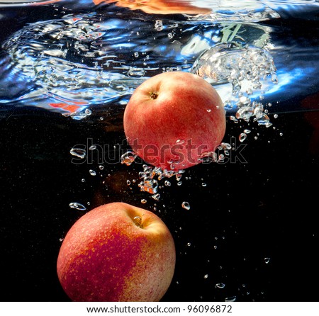 two apple fell into the water by raising bubbles. On a black background