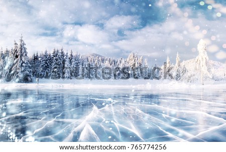 Blue ice and cracks on the surface of the ice. Frozen lake in winter mountains. It is snowing. The hills of pines. Winter. Carpathian Ukraine Europe.
