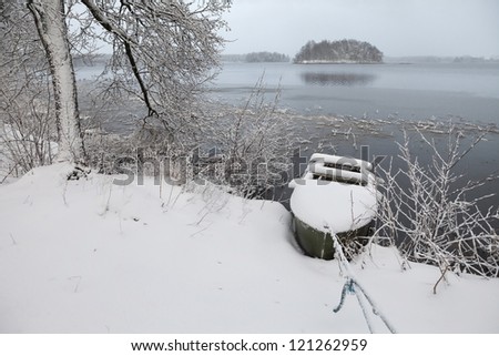 Snow-covered lake shore , falling snow, trees and  boat tied to the shore