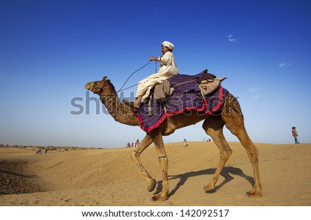 JAISALMER, INDIA - FEB 25: Cameleer waits for tourists at Sam Sand Dune on Feb 25, 2013 in Jaisalmer, India. Apart from farming, camel riding activity is another income source for desert villagers