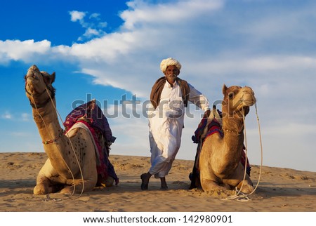 JAISALMER, INDIA - FEB 26: Cameleer and his herd at the Sam Sand Dune on Feb 26, 2013 in Jaisalmer, India. Apart from farming, camel riding activity is another income source for desert villagers