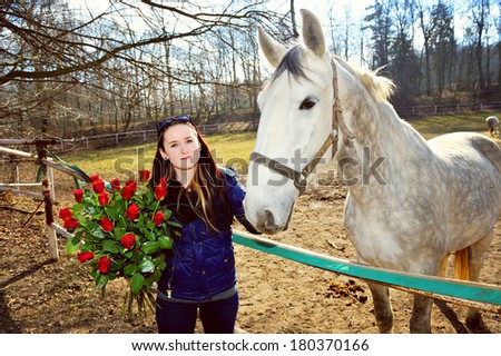 Beautiful young woman standing with bunch of roses before white horse
