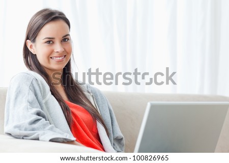 A half length shot of a woman smiling as she looks into the camera with her laptop