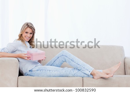A woman who is smiling at the camera is sitting on a couch is holding a pink box