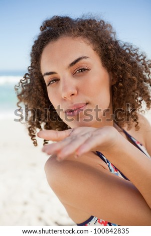 Young woman sending a kiss while gently blowing on her hand on the beach