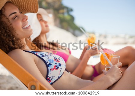 Woman sitting in a deck chair with a friend at her side while holding her cocktail