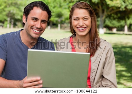 Two friends happily looking ahead as they hold a tablet in a sunny grassland