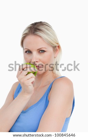 Blonde woman holding an apple close to her mouth against a white background
