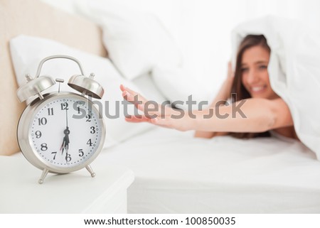 The woman reaches out to silence her alarm from under the quilt.