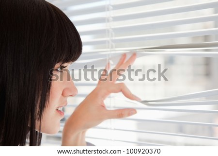 A woman at the window as she looks out through the blinds