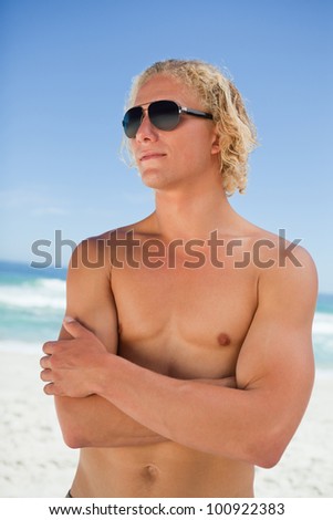 Blonde man looking towards the side and standing on the beach with arms crossed