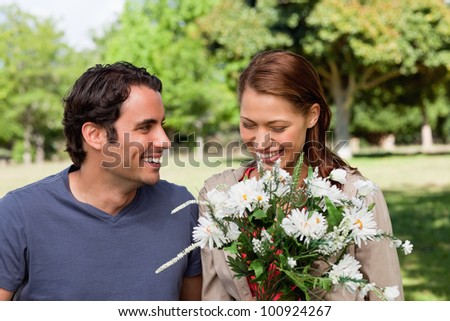 Woman joyfully looking at a bunch flowers as she is being watched by her friend who is smiling in an open grassland area