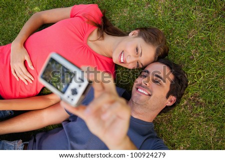 Man taking a photo of him with his friend while lying side by side on the grass