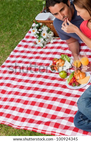 Young woman feeding her friend as they lie next to each other on a blanket with a picnic basket and food