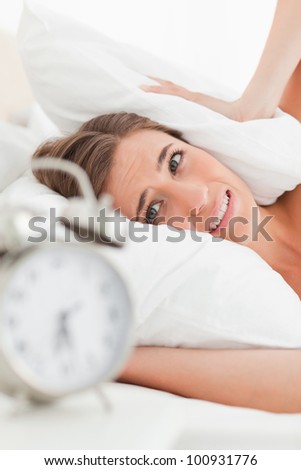 A close up shot of the woman with a pillow over her ears to drown out the alarm.