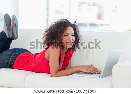 A woman with a laptop on the couch, smiles with her legs raised up, while looking forward.