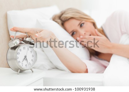 A woman in bed yawning and reaching over to silence the ringing alarm clock beside her bed.