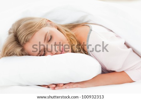 A woman resting in bed with her head on the pillow and her hands underneath it and her eyes are closed.