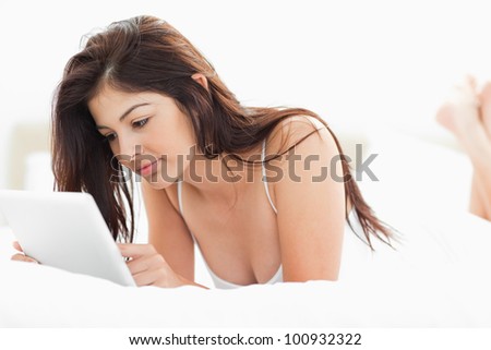 A woman using a tablet pc while lying on a bed with her legs crossed.