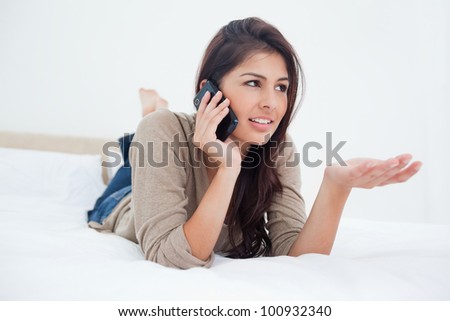 A woman with her hand held out, her legs crossed and making a phone call while lying on the bed.