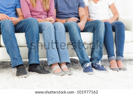 A half length shot of four pair of feet with their owners sitting on the couch