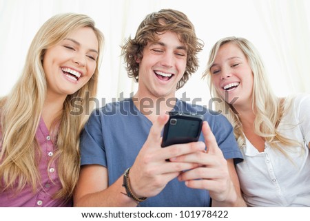 Three smiling friends sit together and look at the message on the man\'s mobile phone