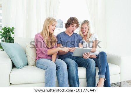Three friends looking at the screen of the tablet and looking shocked as the girls point at the screen