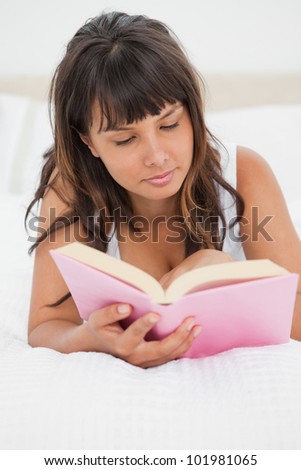 Young woman reading a pink book in her white bed
