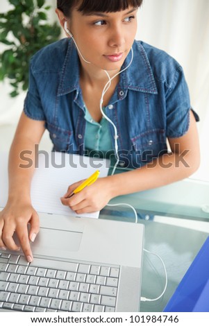 Female student looking away while doing her homework and listening music