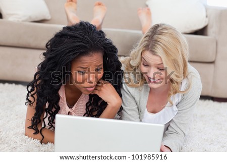 Two women are lying on the ground and using a laptop