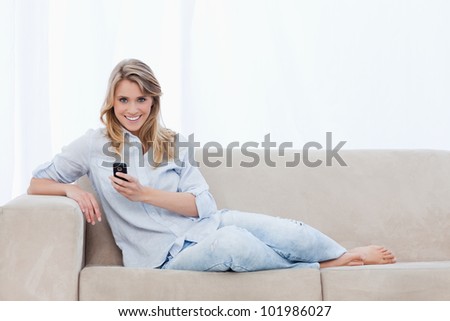 A woman sitting down on a couch is holding a mobile phone and smiling