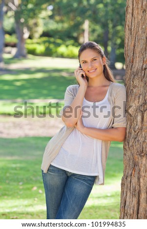 Smiling young woman on her cellphone leaning against a tree