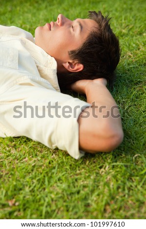 Side view of a man lying in grass with his eyes closed and his hands resting underneath his head