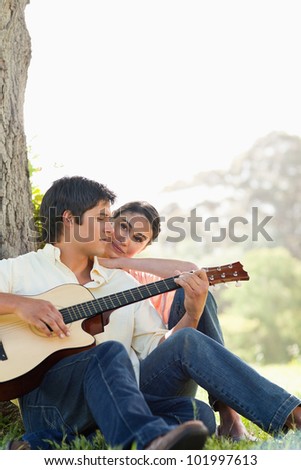 Man looking downwards while playing the guitar as his friend watches him