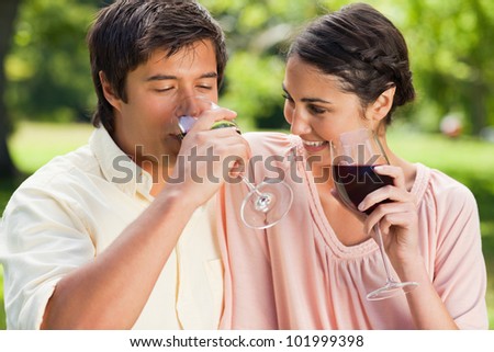 Man drinks a glass of red wine while his friend is looking at him in a park
