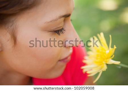 Woman closing her eyes while smelling a yellow flower with grass in the background