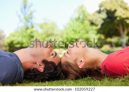 Two friends smiling with their eyes closed as they lie head to head on the grass