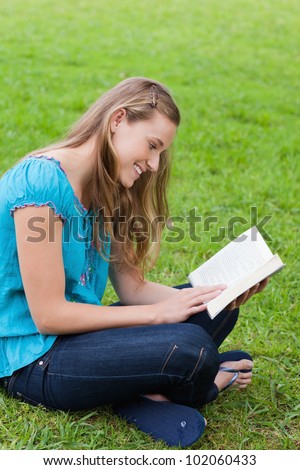 Happy young girl reading a book while sitting cross-legged on the grass in a park