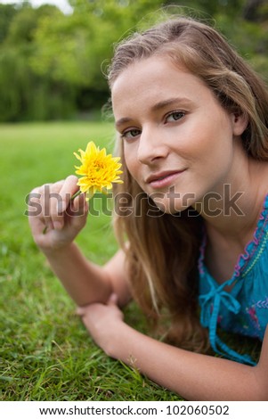 Young relaxed girl lying on the grass in the countryside while holding a yellow flower
