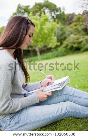 Side view of a young student sitting in a park while seriously writing on her notebook