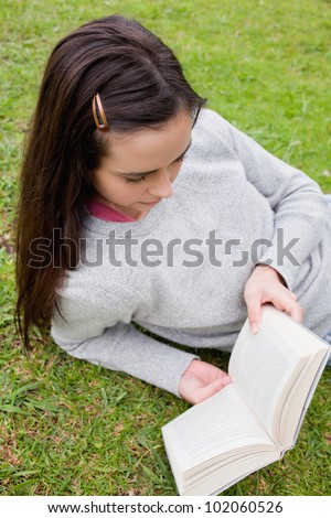 Young serious woman reading a book while lying down in a public garden