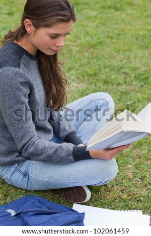 Relaxed young girl reading a book while sitting down on the grass in the countryside