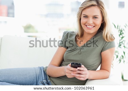 A woman lying on the couch smiles as she uses her phone while looking forward.