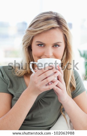A close up shot of a woman looking forward, as she holds a mug up in front of her mouth.