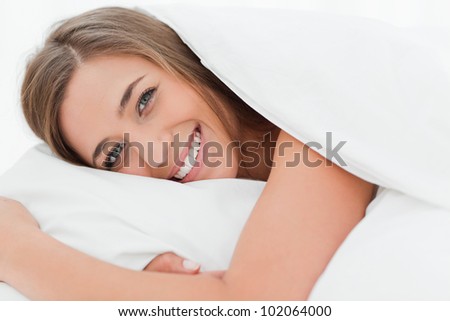 A close up shot of a woman in bed smiling as she has her head on the pillow.
