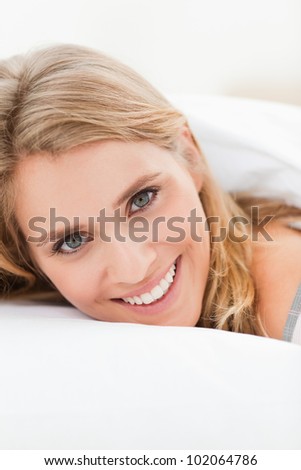 A close up shot of a woman lying in bed smiling, with her head slightly raised but still on the pillow.