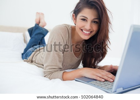 A smiling woman with her legs raised slightly in front of her laptop lying on the bed.